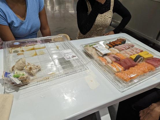 One empty and one nearly full plastic covered tray with sushi