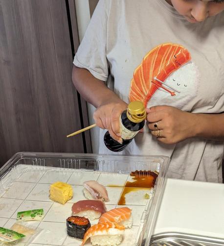 A nearly empty plastic tray and a kid pouring soy sauce in one corner. A few pieces of nigiri sushi are on the tray.