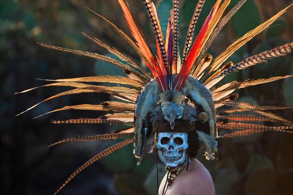 Personne portant un masque rituel maya, figurant une tête de mort entourée de longues plumes