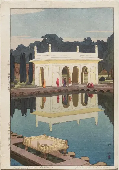 A small white building with arched openings in front and sides with a large rectangular pond that reflects the building and some ladies in sarees who are in front of the building and trees in the background. 