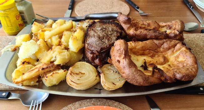 A serving tray loaded with roast beef roasted onions, roasted potatoes, Parsnips, and Yorkshire puddings. 