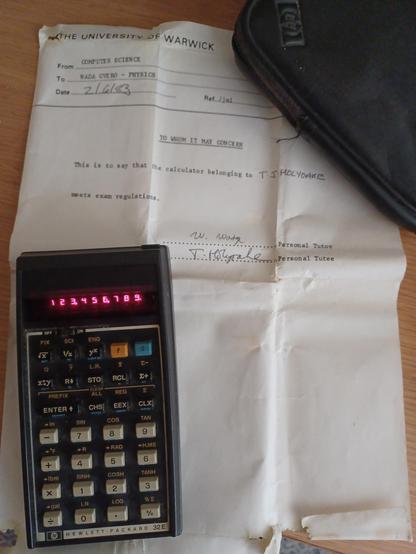 A HP32E calculator displaying 123,456,789. It is sitting on a University of Warwick internal memo, signed by me and my personal tutor, declaring that it meets exam regulations. The case for the calculator is partly shown in the top right corner of the image.