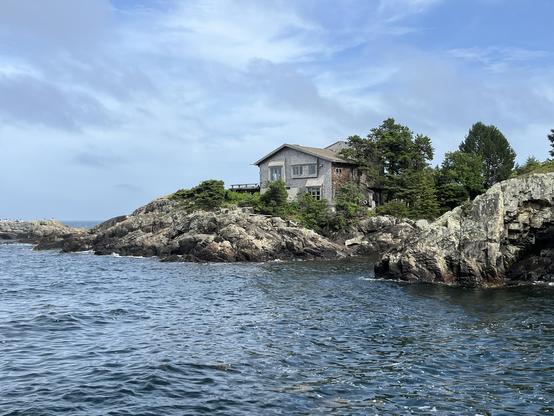 Shingled Cape Cod style house sitting on rocky outcrop over a tiny Atlantic inlet. 