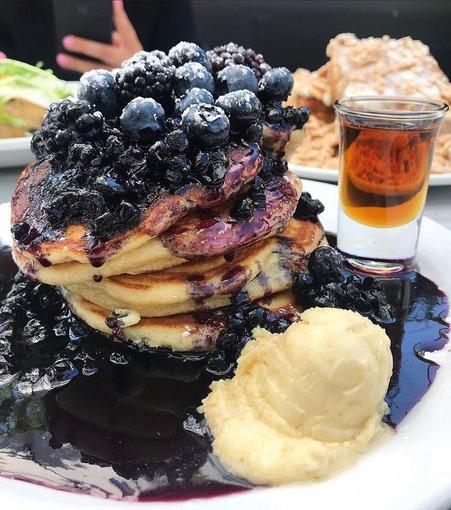 massive blueberry pancake stack with tons of blueberries on top with  blueberry sauce and vanilla ice cream and a shot of whiskey. 