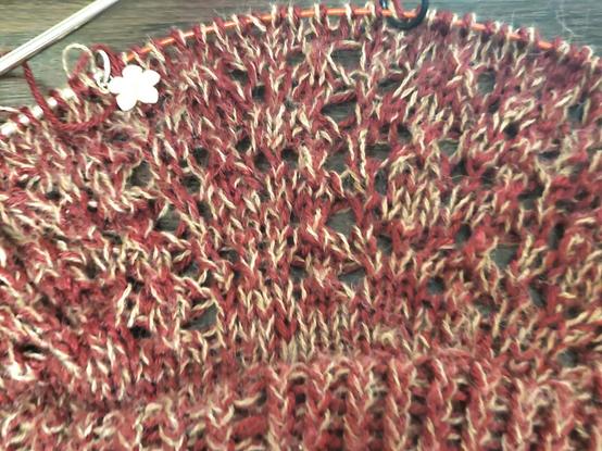 Close up of lace pattern on yoke, burgandy and camel yarns held together, the fabric is on circular needles with pink enamel flower charm on needle noting beginning of row. Pattern is hard to read now but will be visible once blocked. I know, because I swatched <pats self on back>