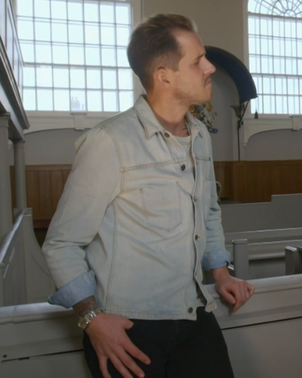 British Historian Dan Jones seen to advantage wearing an acid-washed denim button-up with the sleeves cuffed over a white crew neck and black slacks. His hair is styled in a pompadour and he's leaning on a railing in an ancient courtroom, lookin' like a fine ass greaser from the fifties.