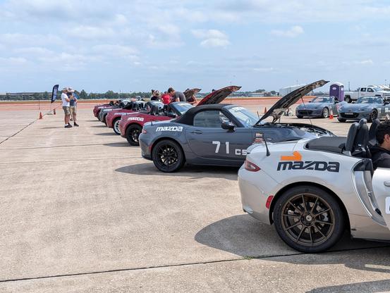 Several 4th generation Miatas parked at an angle on a concrete surface. They all have Mazda stickers and magnetic numbers to identify the cars.