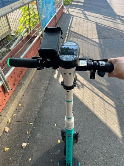 The view from standing on one of the electric scooters. A quiet road is ahead and you can see the handle bars and pole extending down to the wheels and kickboard. 