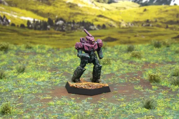 A painted miniature of a Stinger 'Mech.  Its upper body is purple, and its limbs are dark green camo.  It has no emblems or other markings.  The miniature is photographed on grassy terrain.