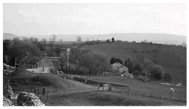 Grainy black and white film photograph showing rolling fields with hills in the distance.