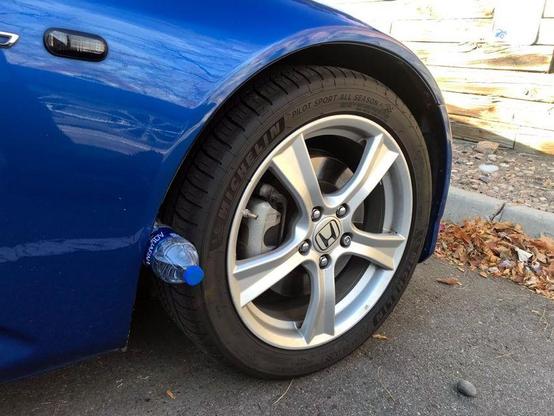 Une bouteille en plastique coincée entre le pneu et le passage de roue à l'avant gauche d'une voiture bleue