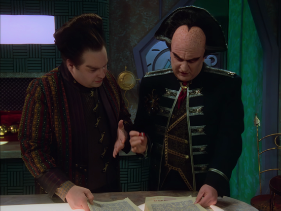 Two men, Vir and Londo, standing over a desk with papers on it. They are both gesturing with their hands, discussing the content of the documents.