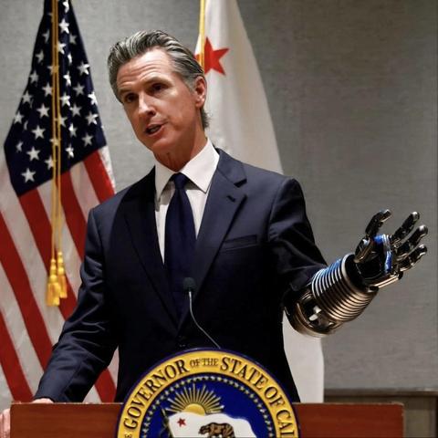 California Governor Gavin Newsom in a suit and tie stands confidently at a podium, wand gestures with his robotic arm, as he addresses an audience with a focused expression. The seal of the Governor's office on the front of the podium, the American flag and California flag are behind him.