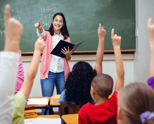 Une enseignante fait la classe devant de jeunes élèves levant le doigt pour répondre