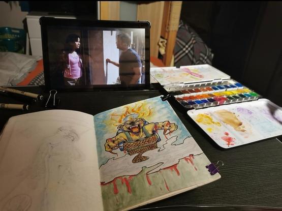 Picture of my bed-desk with my sketchbook, pens, watercolor and my tablet in front of me, playing Dexter