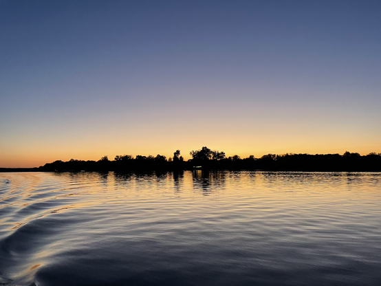 Line of orange sunset light behind the trees reflects off the dark water. 