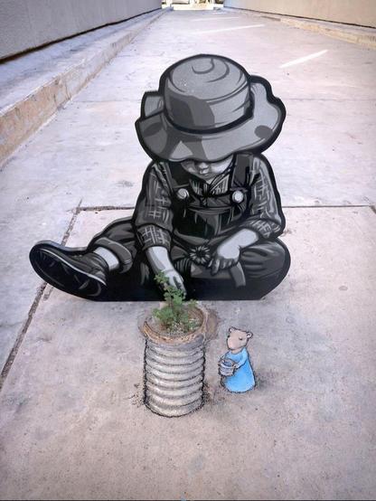 Streetart. A collaboration of chalk art and paper stencil art. A little mouse (named Nadine) with a bucket of water and a tin can were drawn with chalk on a gray sidewalk. There are weeds growing on the ground that have been integrated into the drawing and it looks like a plant is growing out of the can. Behind it, another artist (Joei Urato) has placed a drawing of a child sitting on the ground as a cardboard stand-up. The child in dungarees and a sun hat holds a small flower in his hand and looks at the growing plant with his mouse.