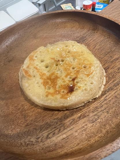 A sourdough crumpet, covered in butter, on a wooden plate. 