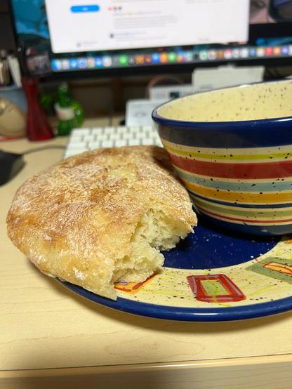 Half a sourdough loaf on a plate next to a bowl (that contains soup). The plates are brightly coloured. 