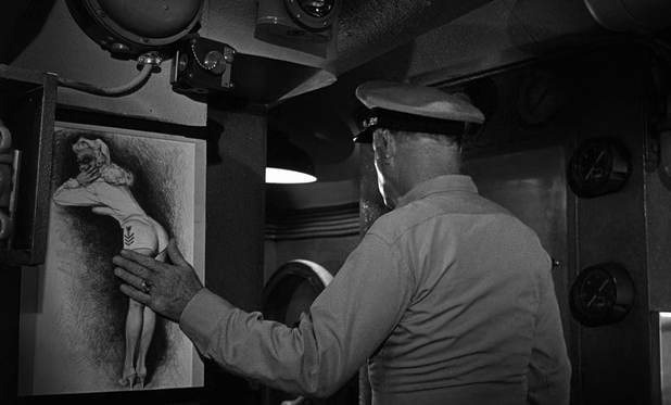 A black and white medium shot of World War II American Navy officer patting a poster showing a uniformed pin up girl with her tushy up in the air as he steps through a door.