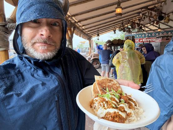 I’m wearing a rain coat, beaded with water, while holding a plate of chicken tika masala with rice and pita.