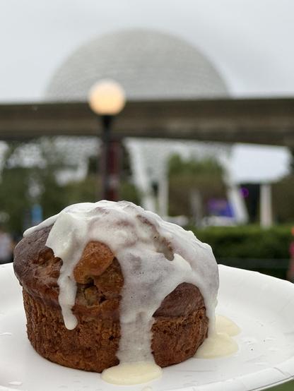 A small carrot cake covered with icing poses in front of an out-of-focus Spaceship Earth.