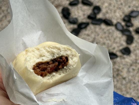 A chicken teriyaki steamed bun with a bite taken out of it. In the background is a Mickey Mouse head outline formed out of black rocks. 