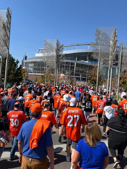 A crowd of people dressed in orange making their way to a nearby stadium.