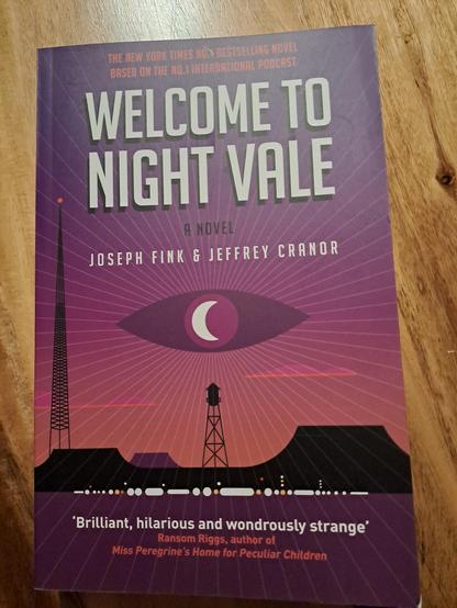 The cover of the book. 

A purple stylised eye radiates lines out from the centre of the image, above a black silhouette of an old fashioned water tower. Beneath it are hills, and to the left a tall radio tower. There is Morse code or something similar along the bottom that I haven't translated...