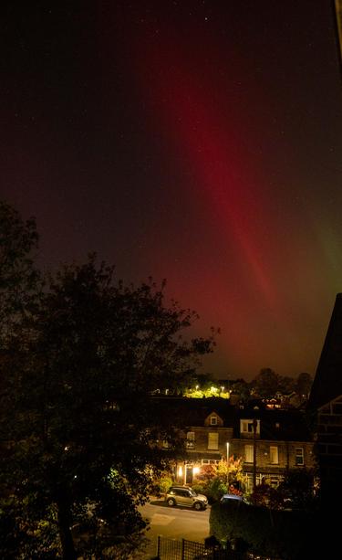 Northern lights, aurora borealis, mainly red streaks with a little green, above houses lit by streetlights.