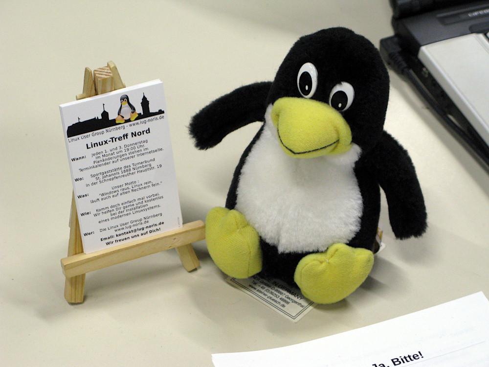 Foto: Ein kleiner Linux-Pinguin sitzt rechts vor einer kleinen Staffelei mit unseren Visitenkarten.