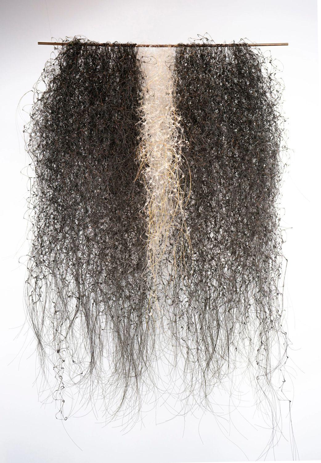 Hanging wall sculpture of thin black and white fibers cascading downward in clusters