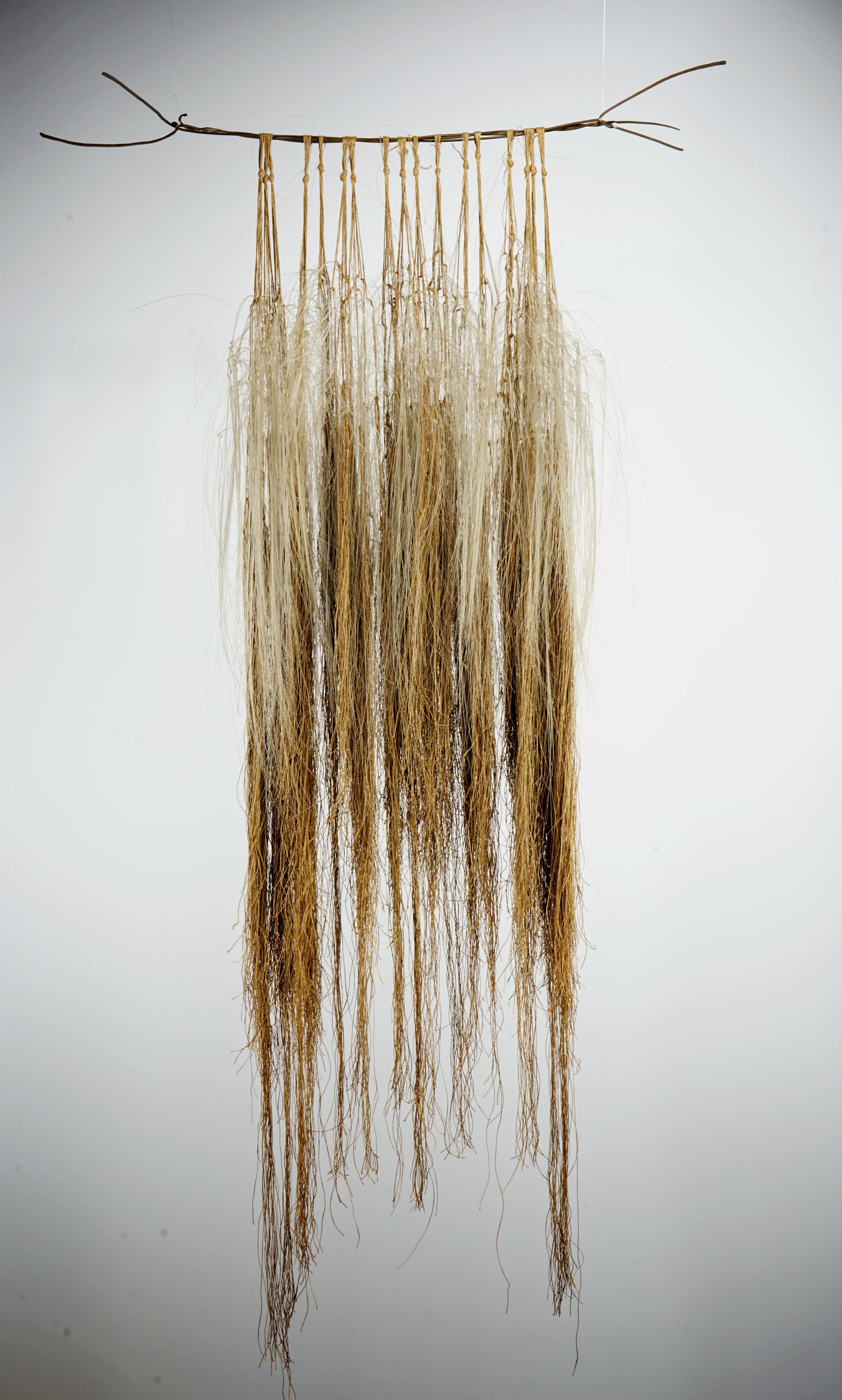 Hanging wall sculpture of thin brown and cream colored fibers cascading downward in long clusters