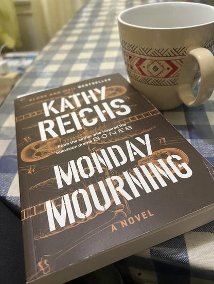 Photo of paperback edition of «Monday Mourning» by Kathy Reichs, with a mug beside...