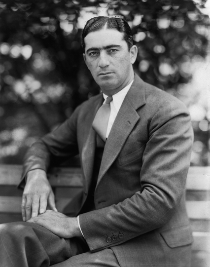 Photo of Berg sitting on a park bench.  He is wearing a suit and tie. 