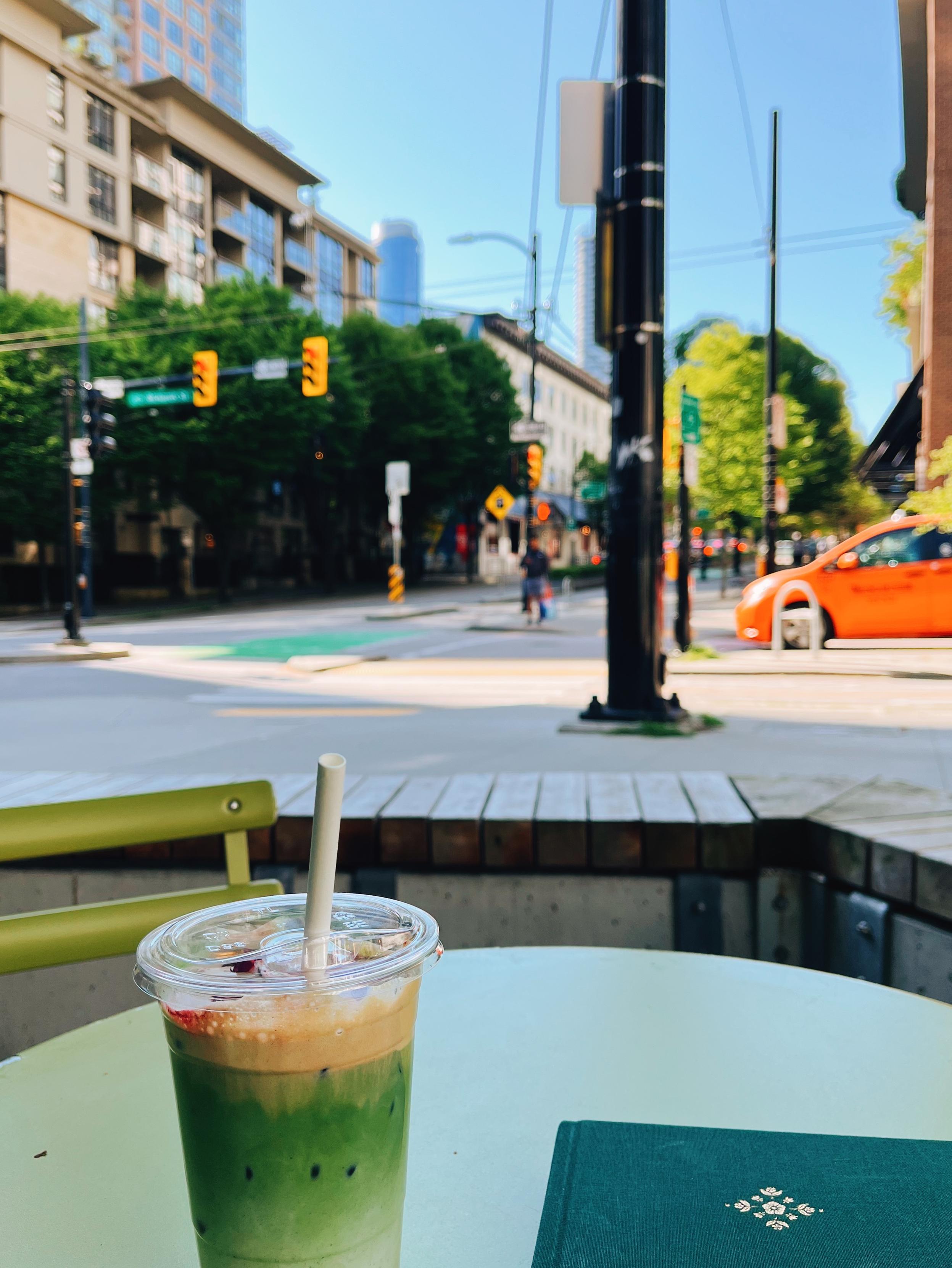 View of a street corner from a cafe patio, where I’ve got an iced matcha and a sketchbook.