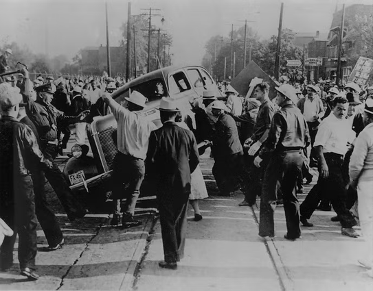 Workers overturn a car in Cleveland during auto workers strike.