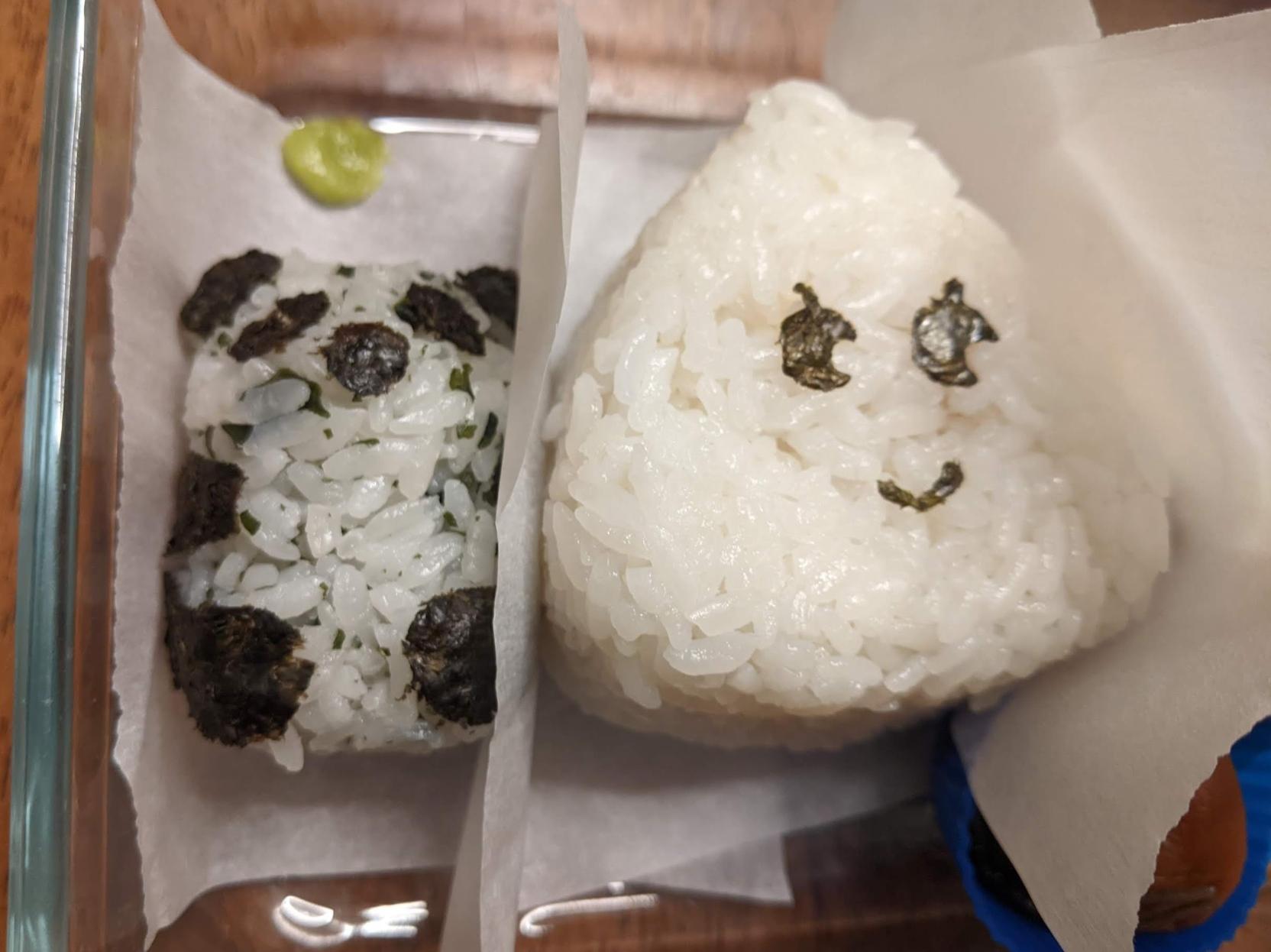 Close up of panda and triangular onigiri with eyes and thin curved smile of nori