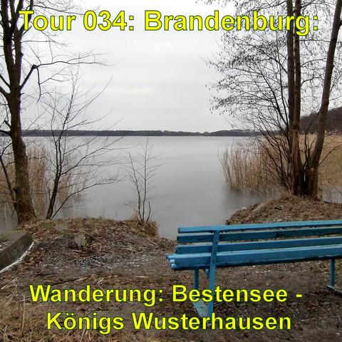 Ruhige Seelandschaft an einem trüben Tag. Im Vordergrund steht eine blaue Bank, die zum Verweilen einlädt, mit Blick auf das Wasser. Einige kahle Bäume und Büsche umgeben die Bank, und man kann sehen, dass das Laub gefallen ist. Der See selbst ist ruhig und spiegelt den grauen Himmel wider. Im Hintergrund sind schwach die Umrisse einer gegenüberliegenden Uferlinie zu erkennen.