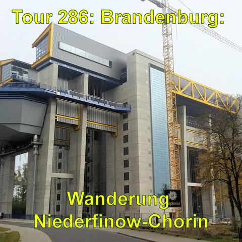 Ein großes, modernes Schiffshebewerk Niederfinow mit mehreren sichtbaren Ebenen und auffälligen gelben Stahlträgern. Die Struktur kombiniert Beton- und Glaselemente und wirkt sehr massiv. Im Hintergrund ist ein teilweise bewölkter Himmel und ein Baukran, was auf andauernde Bauarbeiten oder Erhaltungsmaßnahmen hindeutet. Vor dem Hebewerk sieht man eine gepflasterte Straße, die auf eine Oeffentliche Zugänglichkeit schließen lässt. Die umgebenden Bäume tragen herbstliches Laub.