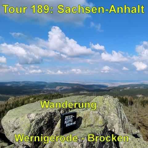 Aussicht von einem Gipfel mit großen Felsen im Vordergrund über einen ausgedehnten Wald und Hügellandschaft. Auf dem Felsen sieht man den schwarzen Kasten mit dem Gipfelbuch der Zeterklippe. Darüber ein klarer Himmel mit einigen Wolken.