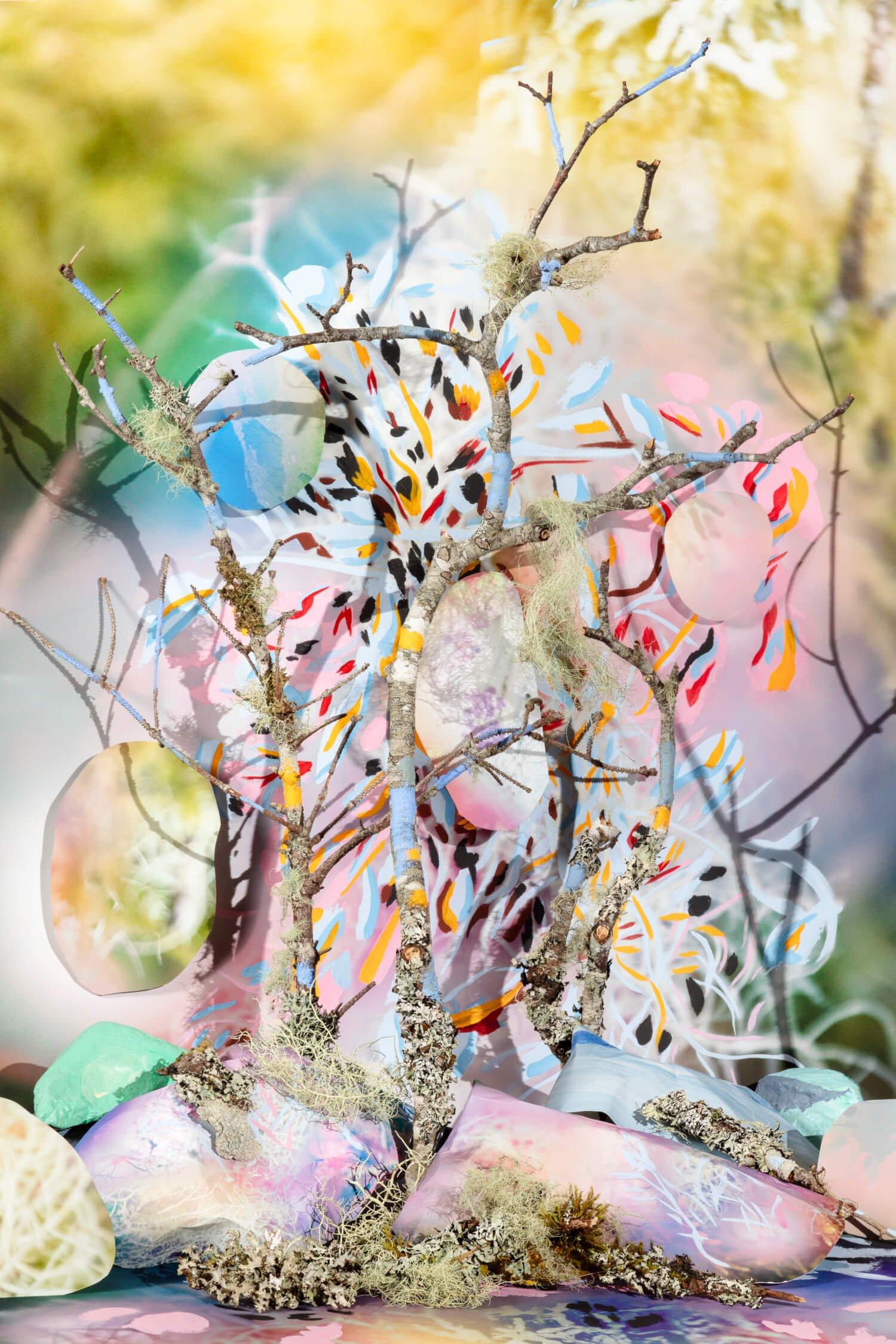 Mixed media tableau in soft colors with upright twigs placed within painted rocks and paper cut outs.