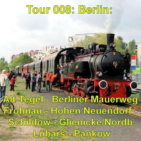 Eine historische Dampflokomotive steht auf einem Gleis, umgeben von Menschen, die die Szene betrachten. Die Lokomotive ist schwarz mit roten Details, aus dem Schornstein steigt Rauch auf. Mehrere Waggons sind an die Lokomotive gekoppelt. Einige Personen, darunter Bahnmitarbeiter in orangenen Westen, stehen nahe der Lokomotive, während andere Passagiere ein- und aussteigen. Im Hintergrund sind moderne Wohngebäude zu sehen, die einen Kontrast zur nostalgischen Lokomotive bilden. Die Stimmung ist …