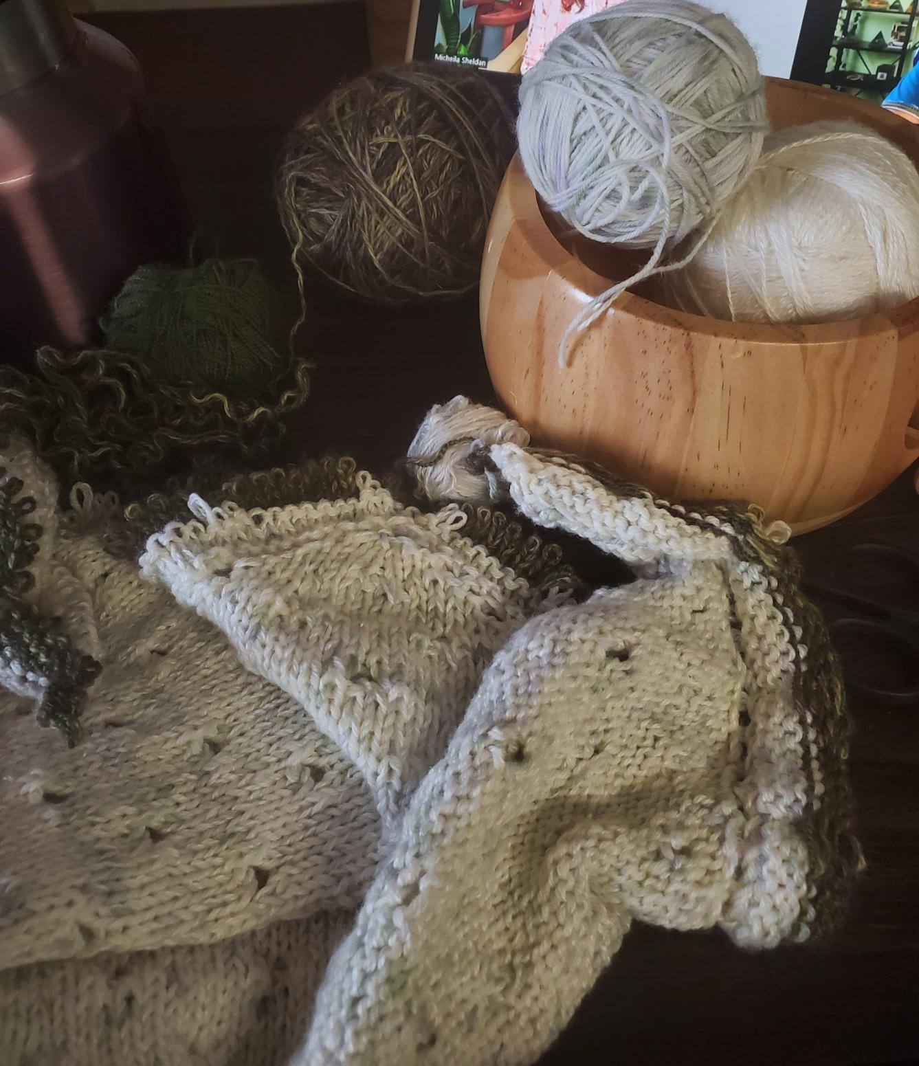 Back side of a mostly white shawl and four balls of yarn, partly frogged