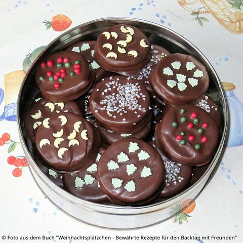 Mit Schokolade überzogene und mit Zuckerdekor bestreute Ischler Weihnachtsplätzchen in der Blechdose.