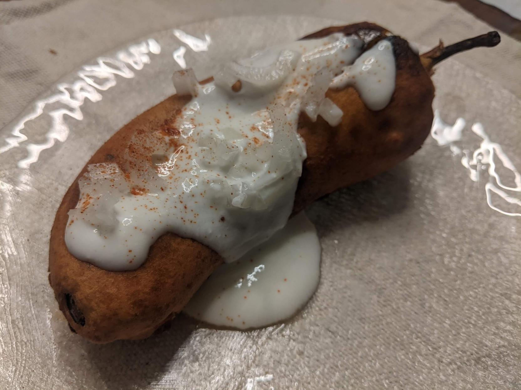 Besan battered Chilli (Hungarian kind so not totally mild like banana ones) on a plate with a yogurt based sauce, chopped onions, and sprinkle of cayenne + paprika