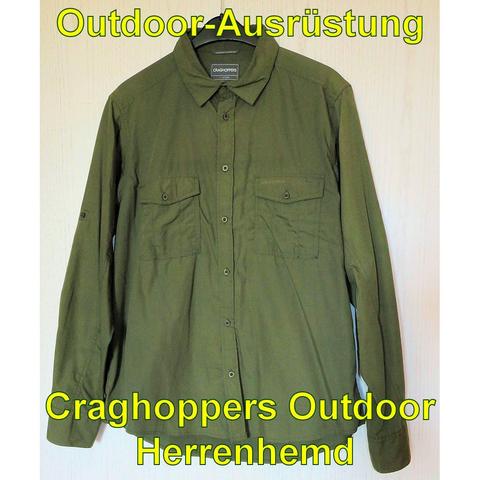 Ein olivgrünes, langärmliges Outdoor-Herrenhemd der Marke Craghoppers hängt an einem Bügel. Das Hemd hat zwei Brusttaschen mit Knöpfen und eine durchgehende Knopfleiste. Die Ärmel sind hochkrempelbar und können mit einer Lasche fixiert werden. Der Stoff wirkt leicht und atmungsaktiv, ideal für Outdoor-Aktivitäten wie Wandern.