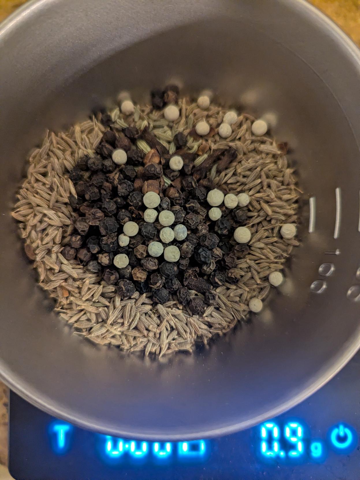 Metal bowl with cumin seeds, cloves, black peppercorns, and some white pepper