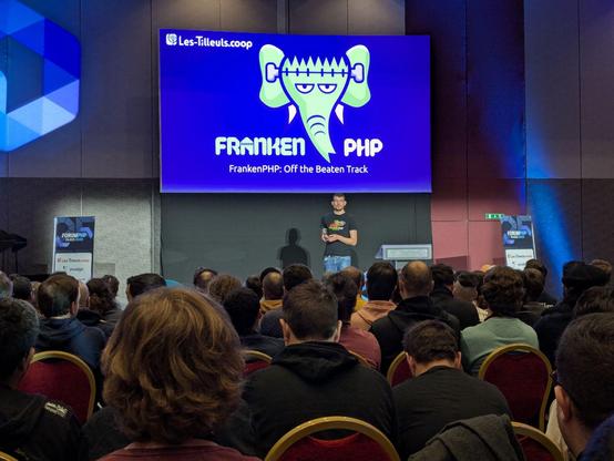 There is a man giving a speech in front of a seated audience