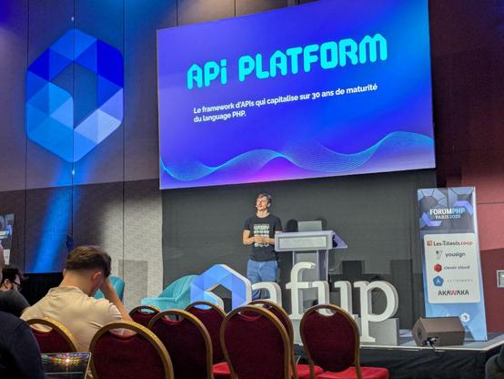 There is a man giving a speech in front of a seated audience